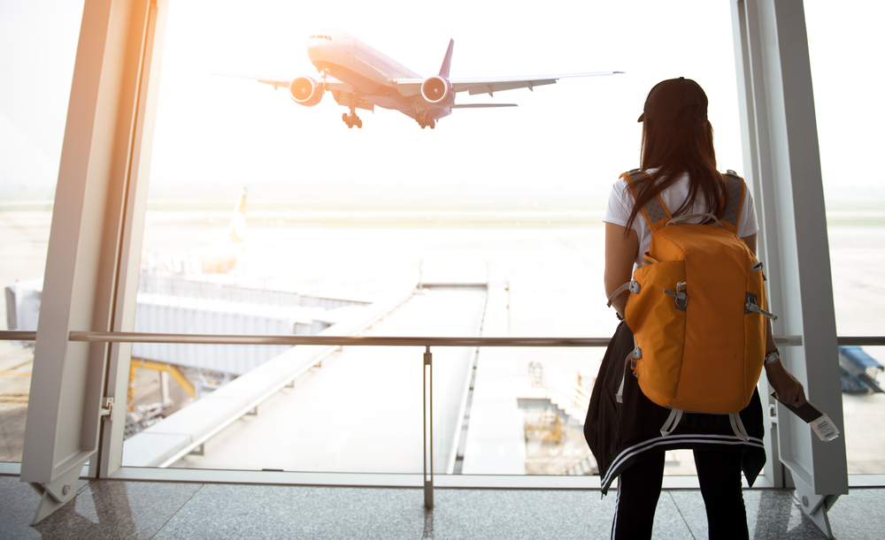 Mulher de costas olhando um avião decolar