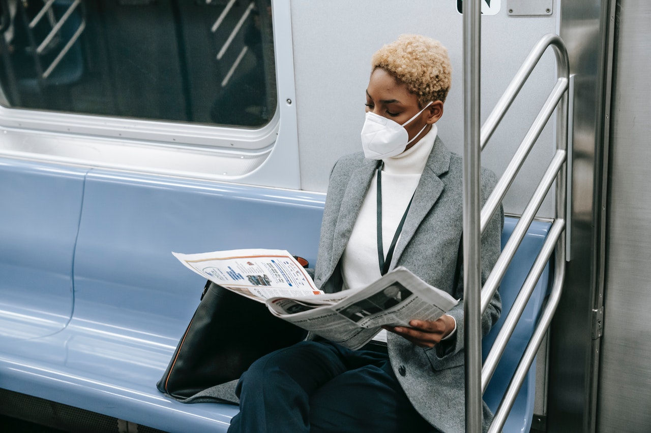 Mulher lê as notícias da semana no jornal em papel dentro do metrô