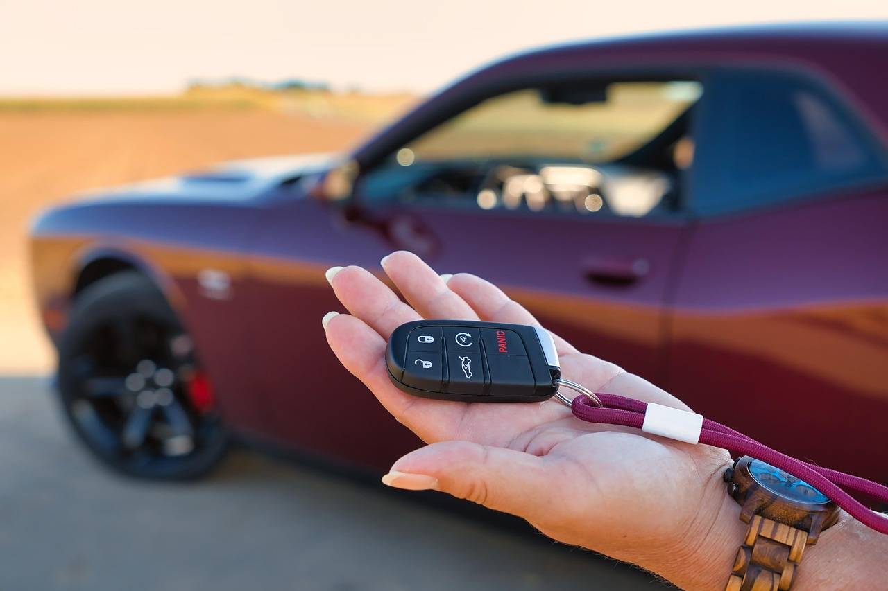 Mão feminina com chave de carro e veículo ao fundo