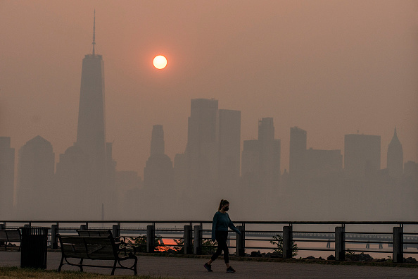 Uma mulher caminha enquanto o sol nasce atrás do One World Trade Center e do horizonte de Nova York, enquanto a fumaça dos incêndios florestais do Canadá cobre o distrito de Manhattan, visto do Liberty State Park, em 8 de junho de 2023 em Nova Jersey (Eduardo Munoz Alvarez/Getty Images)