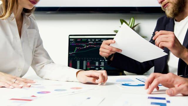 Duas pessoas sentadas em lados opostos da mesa com um gráfico de fundo