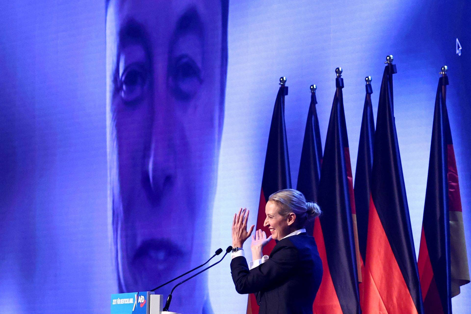 Alice Weidel, colíder do AfD, aplaude enquanto Elon Musk aparece na tela durante evento de campanha eleitoral em Halle, na Alemanha - 25/01/2025 (Foto: Karina Hessland/Reuters)