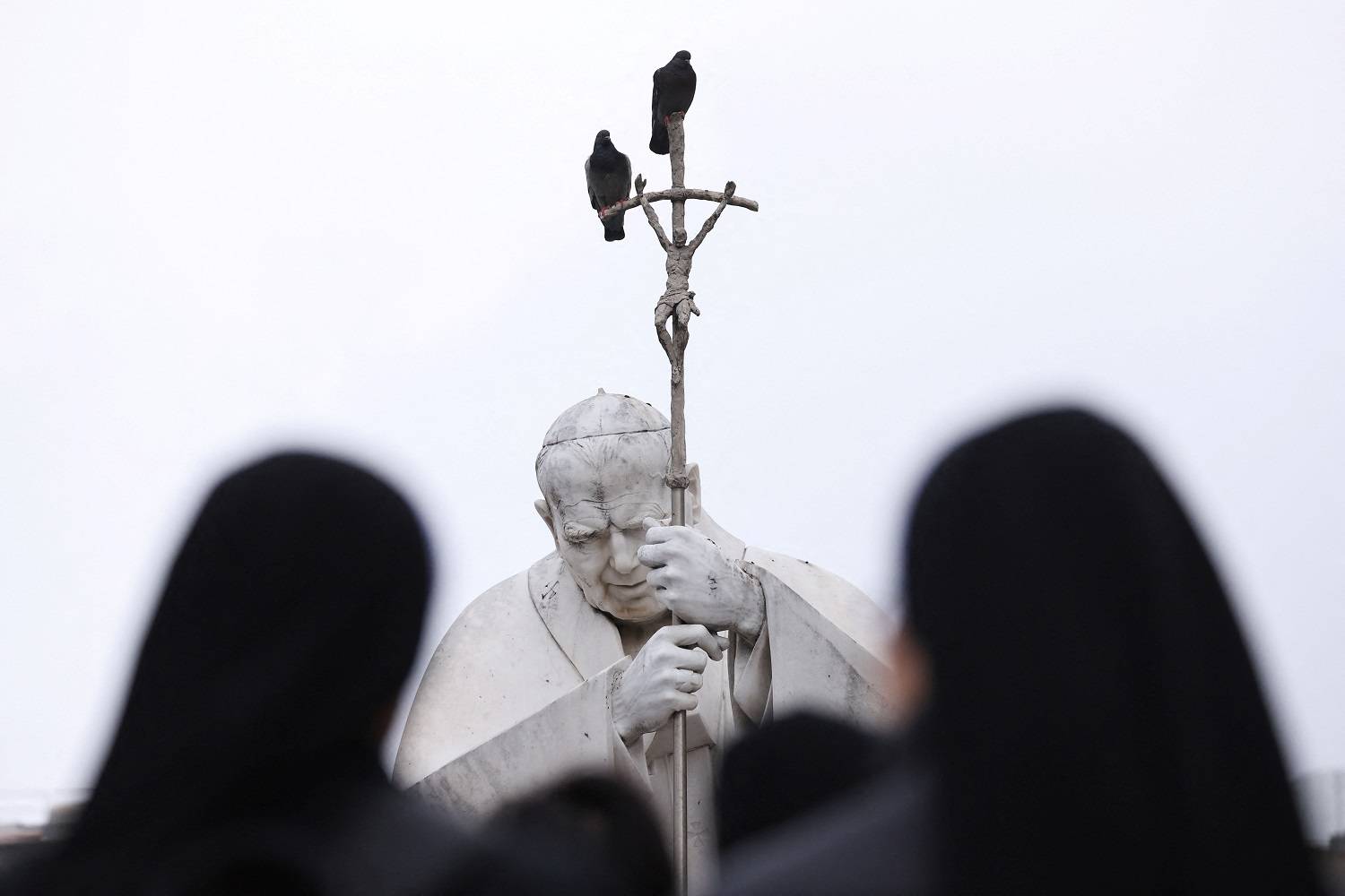 Estátua do falecido papa João Paulo 2º com pessoas rezando do lado de fora do Hospital Gemelli, onde o papa Francisco está internado em Roma
 25/2/2025     REUTERS/Claudia Greco