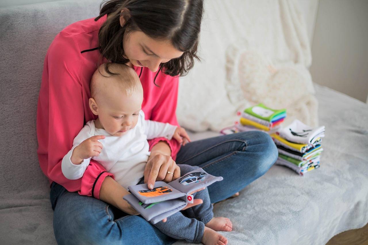 Mulher sentada com bebê no colo lendo livro infantil
