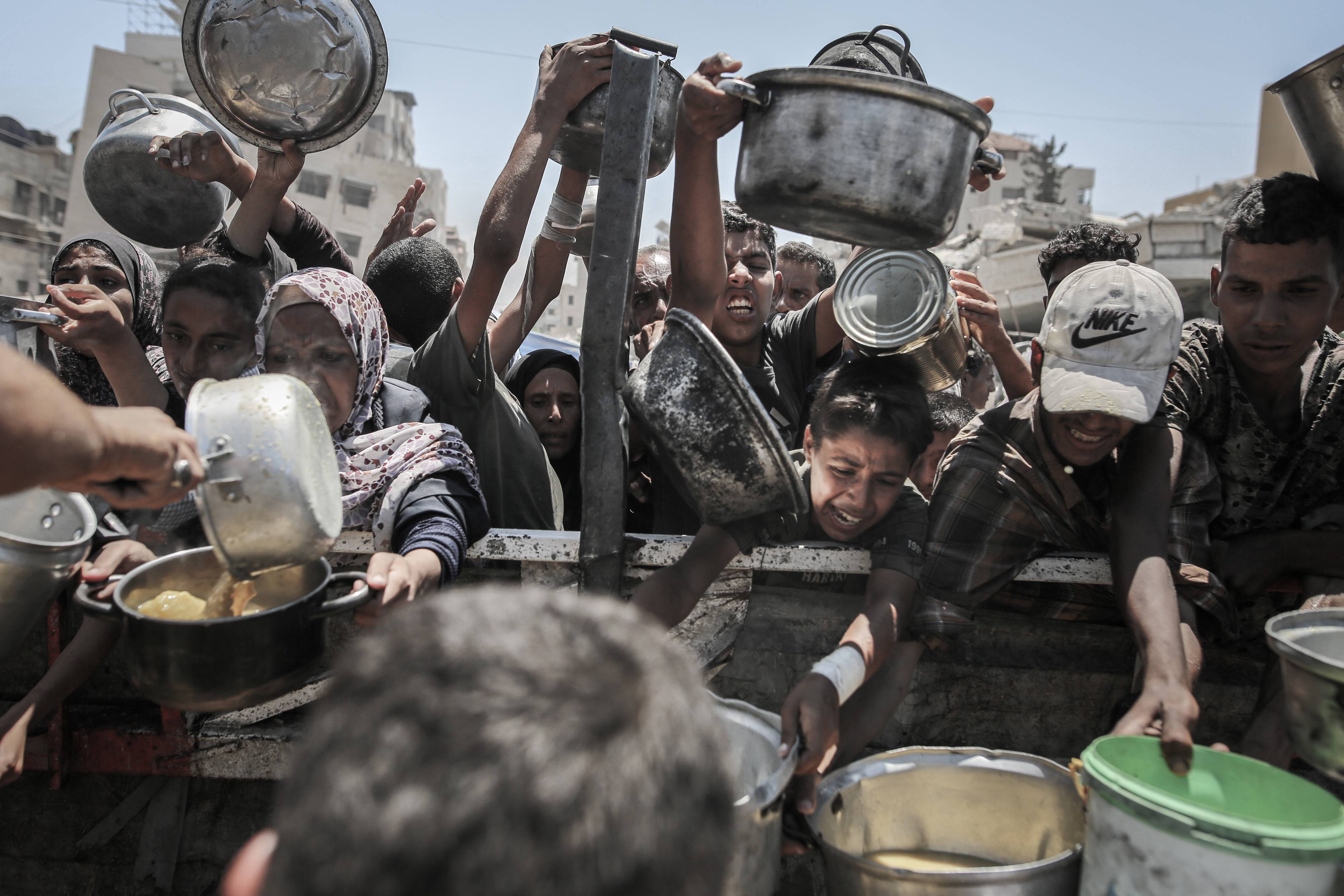 Palestinos tentam arrecadar alimentos em uma cozinha beneficente na Cidade de Gaza. (Foto: Ahmad Salem/Bloomberg)