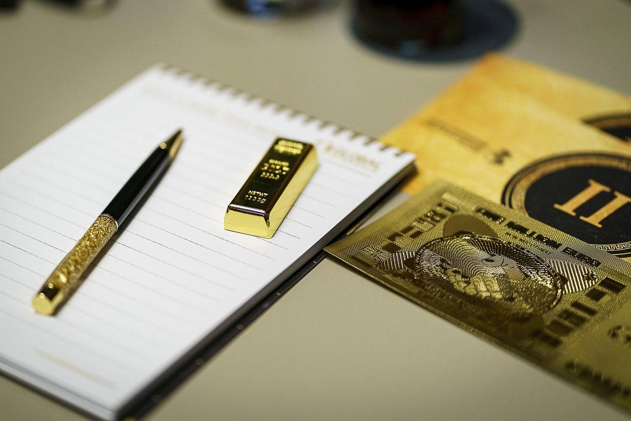 caneta e barra de ouro sobre bloco de notas em cima da mesa